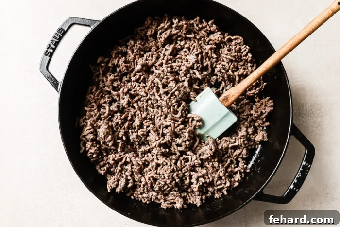 Overhead view of cooked ground beef in a cast-iron skillet, ready to be mixed with vegetables or potatoes.