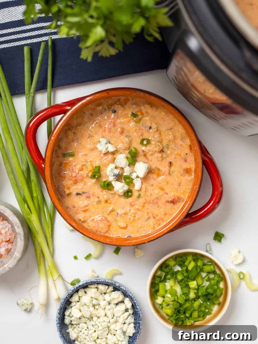 Bowl of creamy Buffalo Chicken Chili topped with crumbled blue cheese and sliced green onions next to Instant Pot.