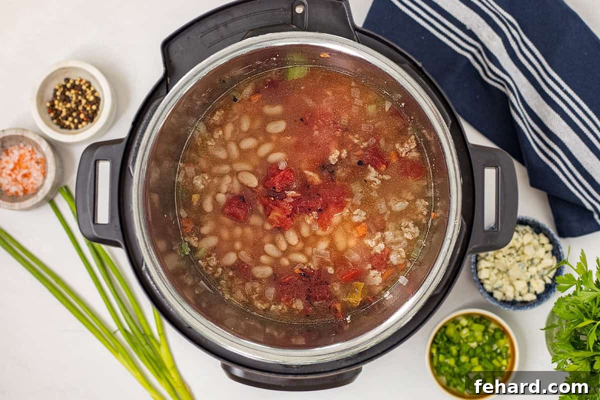 Browned chicken, veggies, broth, white beans, hot sauce, and fire-roasted tomatoes layered inside Instant Pot.