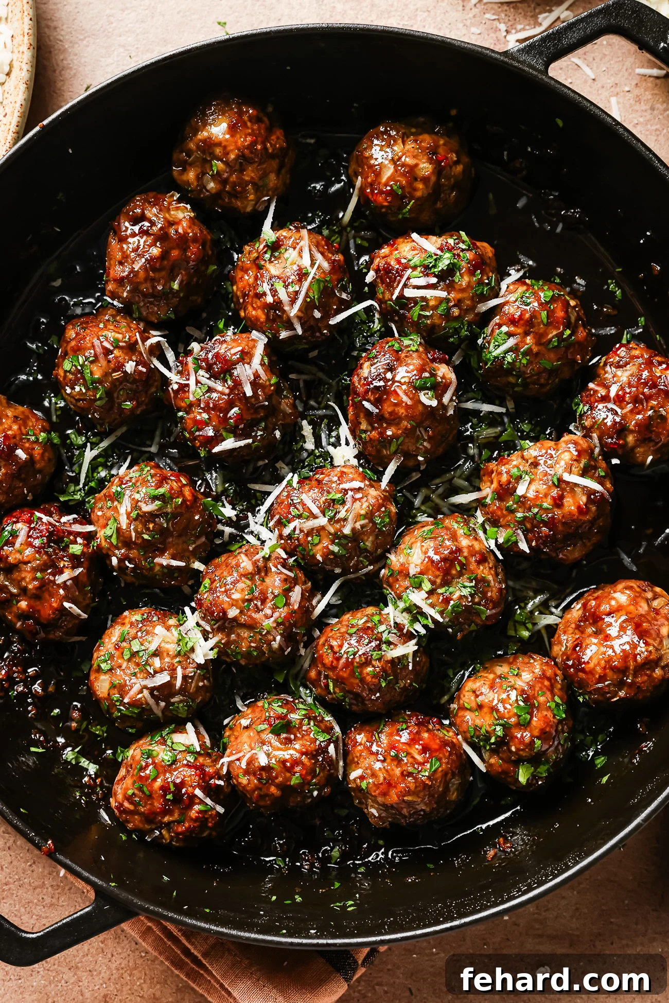 A pan filled with Honey Garlic Meatballs, glazed to perfection and garnished with chopped herbs and grated cheese.
