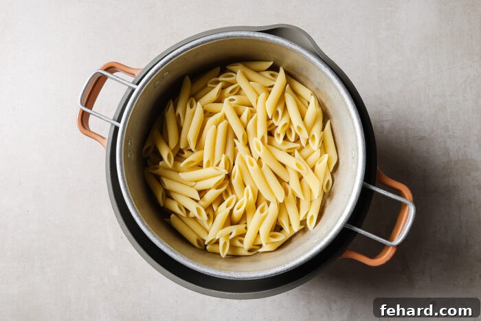 A pot filled with cooked penne pasta, viewed from above, sitting on a light-colored surface.
